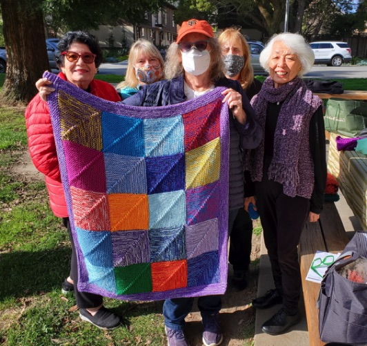 The Knitting Group has met outdoors during the pandemic. Renee, Lois, Bernie, Janet and Chiz gather around a patchwork blanket.